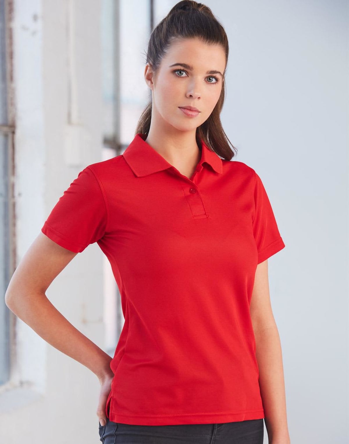 Person in a red polo shirt stands with hand on hip, looking forward.