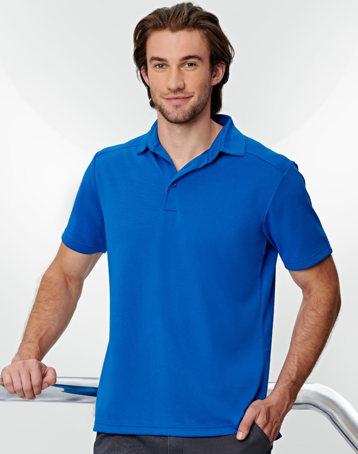 Man in a blue polo shirt standing and smiling against a light background.