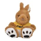 A plush kangaroo toy with brown fur, wearing a yellow shirt with black text. It has large feet with paw print designs. Its ears are upright, and it sits facing forward.