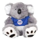 A fluffy gray koala bear plush toy with white ears and a black nose. It wears a blue shirt with a Panadol Baby & Infant logo on its chest. The feet have black paw prints.