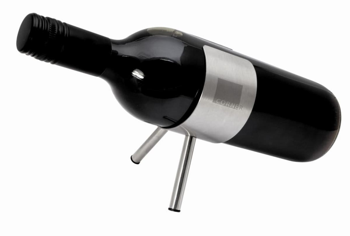 A wine bottle placed horizontally on a minimalistic, silver metal stand with two legs. The bottle appears dark with a cork closure and a modern design. The background is plain white.