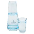 A clear blue glass carafe filled with water stands next to a smaller clear glass half-filled with water. The carafe has a Campfire Industries logo printed on it.