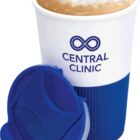 A cup of coffee with frothy milk sits in a white and blue reusable cup. The cup features a logo with the text Central Clinic and an infinity symbol. The blue lid is placed in front of the cup.
