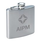 A stainless steel hip flask with a textured finish, featuring the engraved letters AIPM and a star-like logo design above it. The flask has a rounded bottom edge and a screw-on cap attached by a hinge.