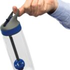 A person in a blue shirt holds a clear water bottle with a blue and gray lid, using their index finger. Inside the bottle is a black straw and a blue, spherical object. The bottle appears to be tilted upside down.