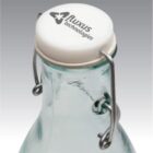 A glass bottle with a flip top closure, featuring the Luxus technologies logo on the white cap. The bottles metal wire lever is visible, securing the cap in place.