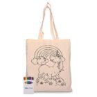 A beige tote bag with an outlined drawing of a unicorn under a rainbow and clouds. The bag is accompanied by a box of crayons, featuring various colors.