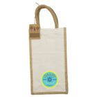 A beige tote bag with brown handles features a blue circular logo with the text Malfy Gin and Italy. A cardboard tag attached to the handle has tree icons and a barcode.