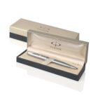 A silver Parker pen rests inside an open beige and black box. The interior is lined with satin fabric, and the box lid is partially visible, displaying the Parker logo.