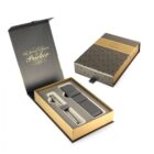 Open and closed Parker pen gift boxes. The open box reveals a pen and leather case inside golden and black packaging. The closed box displays a subtle pattern and Parker logo in gold.