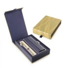 Elegant pen gift set in an open box, featuring a gold pen with a blue leather pouch. The box is blue and gold with abstract patterns, and the brand name is embossed on both the pen and box lid.