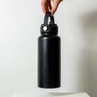 A hand holding the handle of a large black insulated water bottle against a plain white background.