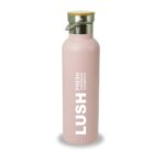 Pink insulated water bottle with a wooden lid and metal handle. The bottle features the text LUSH FRESH HANDMADE COSMETICS vertically in bold white letters.