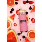 A pink reusable bottle with a bamboo lid and straw lies on a light pink surface surrounded by slices of watermelon, grapefruit, and cherries. The bottle features the words Top Juice and fresh. raw. real.
