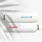Two white cylindrical bottles are placed horizontally on a light surface with palm leaf shadows. The top bottle has HYUNDAI in blue, and the bottom one has Canon in red.