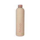 A beige insulated bottle with a pink cap and the word Aēsop vertically printed in pink. The design is sleek and minimalist. The bottle is set against a plain white background.