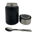 A black and stainless steel insulated food jar set with an open lid and a foldable metal spoon lying in front. The lid has a compact design to store the spoon when not in use.