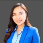 Smiling team member in a blue blazer against a gray background.