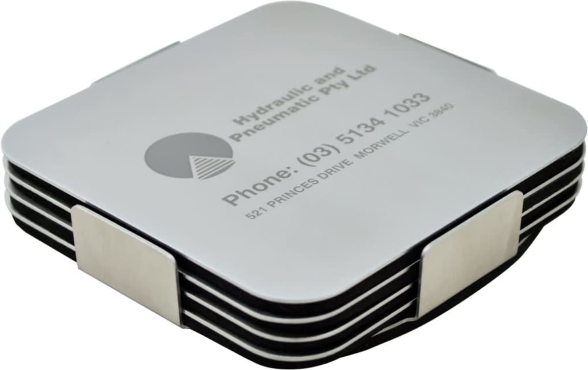 A stack of square coasters with rounded corners, held together by a metal holder. The top coaster has the text Hydraulic and Pneumatic Pty Ltd with contact information printed on it. The coasters have a sleek, modern design.