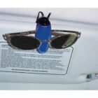A pair of sunglasses is clipped to a cars sun visor using a blue holder. The visor has safety instruction text printed on it.