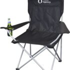 A black folding camping chair with a silver frame, featuring a built-in cup holder containing a bottle. The backrest is branded with a logo and the words water agency.