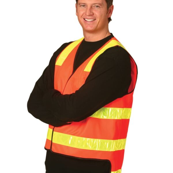 A person wearing a bright orange safety vest with yellow reflective stripes stands with arms crossed. They are smiling and wearing a black long-sleeve shirt underneath the vest. The background is plain white.