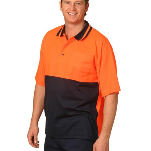 A smiling person wearing an orange and black uniform shirt stands against a plain background. The shirt has a collar and short sleeves.