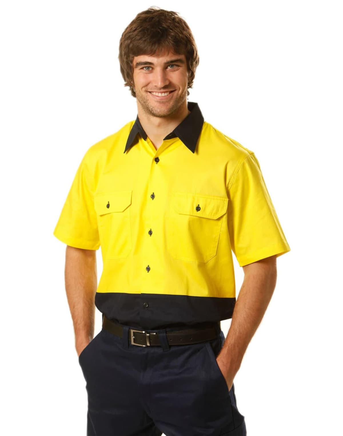A man in a yellow and black collared work shirt with short sleeves stands smiling. The shirt has two front pockets with buttons. He is wearing dark pants and a belt, with his hands in his pockets, against a white background.