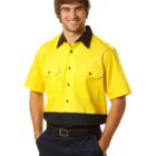 A smiling man wears a short-sleeve, button-up shirt with a bright yellow top and dark blue bottom, along with matching pants. He has his hands in his pockets. The shirt features two front pockets and a contrasting collar.