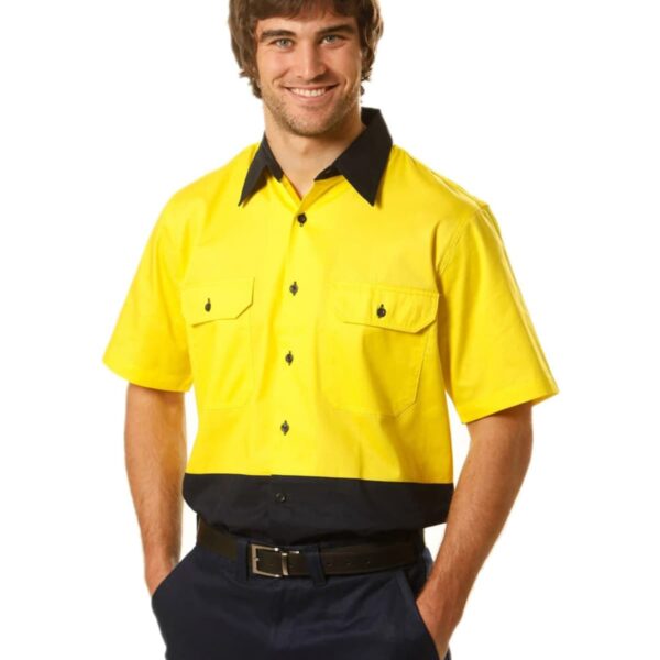 A smiling man wears a short-sleeve, button-up shirt with a bright yellow top and dark blue bottom, along with matching pants. He has his hands in his pockets. The shirt features two front pockets and a contrasting collar.