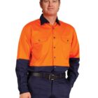 A man wearing an orange and navy work uniform stands with one hand in his pocket. The shirt is bright orange with navy cuffs and collar, and he is wearing matching navy pants.