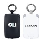 Two portable power banks with keychain rings are shown. One is black with OLI written on it, and the other is white with JENSEN written on it. Both have LED indicator lights at the bottom.