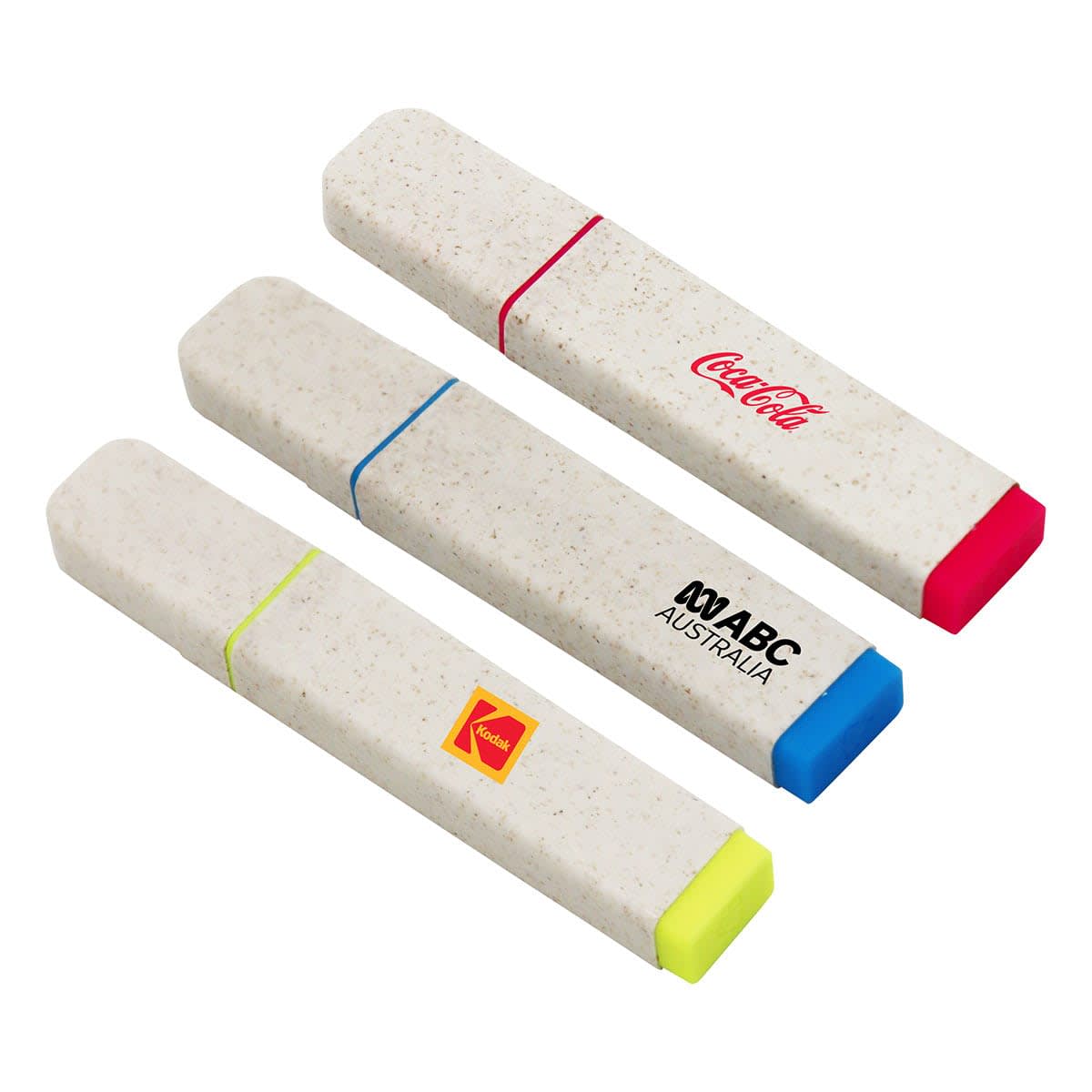 Three rectangular highlighters with rounded edges in beige cases. Each has a colored band and tip: pink with a Coca-Cola logo, blue with an ABC Australia logo, and yellow with a Kodak logo.