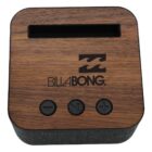 A square speaker with a wood finish on top featuring the Billabong logo. The front has three buttons: power, play/pause, and volume up. The sides are covered in dark fabric.