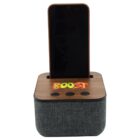 A wooden and fabric speaker with a smartphone docked on top. The word BOOST is colorfully printed on the wood panel. There are three buttons below for audio control. The fabric is a textured dark gray.