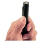 A hand holding a black pen with a built-in compass on the top. The compass displays cardinal directions. The pen has a clip on its side for attaching to clothing or notebooks.