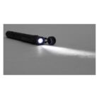 A black penlight lying on a gray surface with its light turned on, casting a focused beam stretching horizontally across the surface. The beam highlights the texture of the surface, creating a stark contrast with the surrounding dim light.