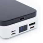A smartphone on a white power bank with digital battery percentage display.