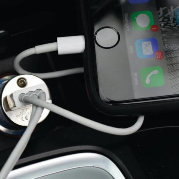 A smartphone connected to a car charger is resting in a vehicles console. The screen shows various app icons and notifications. A charging cable is plugged into the phone and connected to the cars power outlet.
