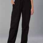 A person is wearing black, loose-fitting sweatpants with hands in pockets. The pants have an elastic waistband with a drawstring. They are paired with a gray top and black sneakers, standing against a plain gray background.