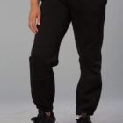 Person wearing black jogger pants and black sneakers, standing with hands in pockets. The background is plain gray.
