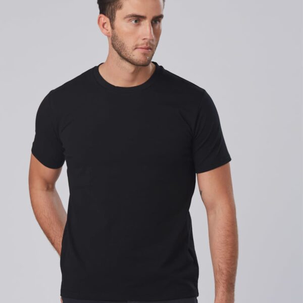 A man with short brown hair and a beard is wearing a plain black t-shirt. He is looking to his left, standing against a light gray background.