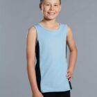 A smiling boy in a light blue sleeveless shirt and black pants stands against a gray background, with one hand on his hip.