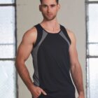 A man in a black sleeveless shirt stands indoors with one hand in his pocket.