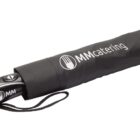 A black folding umbrella partially out of its sleeve, with MMcatering printed in white lettering on the sleeve. The umbrella features a button on the handle and a wrist strap is attached.