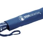 A blue travel umbrella in a matching blue sleeve with the logo MMcatering printed on it. The umbrella has a strap for easy carrying.