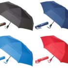 Four umbrellas are displayed, each with a matching carrying sleeve. The umbrellas are black, navy blue, light blue, and red. Each sleeve has a wrist strap and is positioned below the corresponding umbrella.
