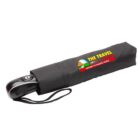 A black travel case with a portable electric device partially visible. The case features colorful text: The Travel Card - Gateway to Raging Gorge, alongside an image of a scenic landscape. A wrist strap is attached to the case.