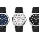 Three wristwatches with black leather straps are displayed. From left to right: a blue-dialed watch with numeric markers, a white-dialed watch with red and black markers, and a black-dialed watch with minimal markers and a small logo.