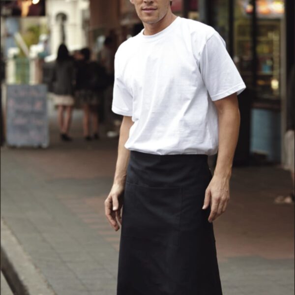 Man standing on a sidewalk wearing a white T-shirt and black apron. The background shows storefronts and blurred figures walking. The word HOSPITALITY is written at the bottom.